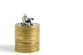 Miniature tiny people toys photography. A poor man or a beggar sit above gold coin stack, isolated on white background