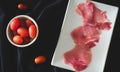 Miniature tomatoes and raw meat on black background