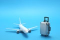 Miniature toy airplane and suitcase on blue background. Royalty Free Stock Photo