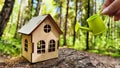 miniature toy house in forest and hand with watering can. natural background. symbol taking care of Eco Friendly home