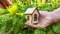 miniature toy house in forest and hand with watering can. natural background. symbol taking care of Eco Friendly home