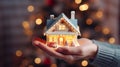 Miniature toy house in hands illuminated by Christmas lights on a luxurious bokeh background. Merry Christmas. Happy Holidays