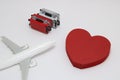 Miniature two suitcases, toy airplane, and a red heart on white background.