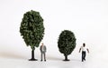 A miniature white man and a miniature black man standing next to a tree of different sizes. Royalty Free Stock Photo