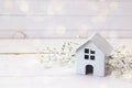 Miniature white toy house with flowers on a white wooden background.