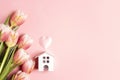 Miniature white toy house with tulip flowers on pink background