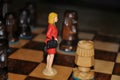 Miniature woman on chessboard between wooden chess pieces