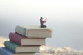 Miniature woman looks at the infinity with the spyglass on a scale of books
