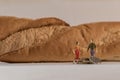 Miniature woman and man figure standing next to big baguette bread and counting coins. Shallow depth of field background. Family Royalty Free Stock Photo