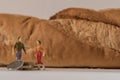 Miniature woman and man figure standing next to big baguette bread and counting coins. Shallow depth of field background. Family Royalty Free Stock Photo