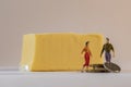 Miniature woman and man figure standing next to big butter brick and counting coins. Shallow depth of field background. Family Royalty Free Stock Photo