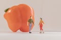 Miniature woman and man figure standing next to big orange bell pepper. Shallow depth of field background. Healthcare, healthy