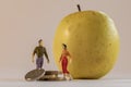 Miniature woman and man figure standing next to big yellow apple and counting coins. Shallow depth of field background. Family Royalty Free Stock Photo