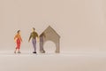 Miniature woman and man figure standing next to house made of coin holder with no coins. Shallow depth of field background. Family Royalty Free Stock Photo