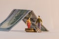 Miniature woman and man figure standing next to house made of dollar bill and counting coins. Shallow depth of field background. Royalty Free Stock Photo