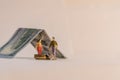 Miniature woman and man figure standing next to house made of dollar bill and counting coins. Shallow depth of field background. Royalty Free Stock Photo