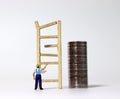 Miniature wood broken ladder and the back of a miniature man pointing there and the pile of coins.