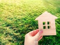 Miniature wooden house on green grass in female hands. Real estate concept. Modern housing. Eco-friendly and energy efficient