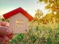 Miniature wooden house in the hands of a man outdoors. Real estate concept. Eco-friendly home. Buying a housing outside the city.
