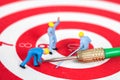 Miniature worker toy on red dart board with green dart Royalty Free Stock Photo