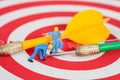 Miniature worker toy on red dart board with green dart Royalty Free Stock Photo