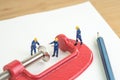 Miniature worker working with red squeezed clamp on notebook with pencil using as budget or financial squeezed, workbench,