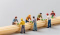 Miniature workers collaborate on a construction project using wooden planks for a creative display Royalty Free Stock Photo