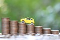 Miniature yellow car model on growing stack of coins money on nature green background, Saving money for car, Finance and car loan