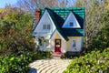 A miniature yellow house with a green roof and a red door in the garden