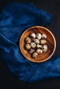 Minimal art of fresh quail eggs in the wooden bowl on the dark background with blue saten or silk around Royalty Free Stock Photo