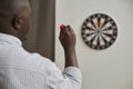 Minimal back view of African American man playing darts and aiming shot