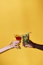 Minimal close up of two hands clinking cocktails against yellow background Royalty Free Stock Photo