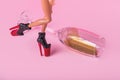 Minimal composition with female doll walking with high heel and spilled champagne glass full of gold glitter on pink background Royalty Free Stock Photo