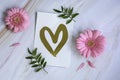 Minimal composition with pink flowers, greeting card with a golden heart and leaves on a marble background. Top view and flat lay