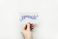 Minimal composition on a white background with girl`s hand holding card with word Sparkle written in calligraphy style. Royalty Free Stock Photo