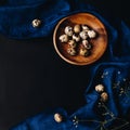 Minimal concept of fresh quail eggs in the wooden bowl on the dark background with blue saten or silk around and dry flowers in Royalty Free Stock Photo