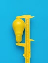 The minimal concept of the idea. A yellow caliper measuring a yellow light bulb on a blue background Royalty Free Stock Photo