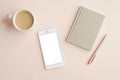 Minimal feminine office desktop with mobile phone mockup with blank screen, cup of coffee, paper notebook and pen on beige Royalty Free Stock Photo