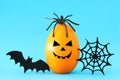 minimal and funny Halloween holiday concept. Orange egg with scary cute face, spiderweb, bat and spider on top. Royalty Free Stock Photo