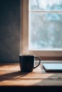Minimal home workstation by window, single slim laptop closed, ceramic mug with steam, light walnut tabletop Royalty Free Stock Photo