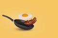 Minimal idea with a frying pan and a flying fried egg and bacon on a yellow background. Creative food concept Royalty Free Stock Photo