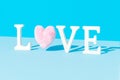 Minimal LOVE word made of white letters and shaggy pink heart against light blue background. Trendy Valentine concept