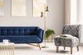 Minimal style living room interior with a navy blue couch, a patterned gray armchair and gold accents of a lamp, a coffee table an