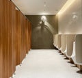 Minimal style and modern beautiful interior design of public restroom with row of urinals, wooden toilet doors, bright light, Royalty Free Stock Photo