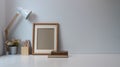 Minimal workspace with frame, pencils, coffee cup, lamp and old book on white table. Royalty Free Stock Photo