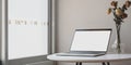 Minimal workspace with open blank screen laptop computer and dry roses vase on white table