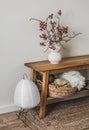 Minimalism scandinavian style interior - paper lamp, cranberry branches in a ceramic vase, basket with blankets on an oak bench in