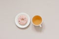 The minimalist banner coffee break. Green tea in a white porcelain Cup and pink donut on a white plate on a beige background. Royalty Free Stock Photo