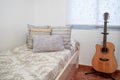 Minimalist bedroom: single bed in light tones, with blue cushions and a guitar. Cozy scene at home Royalty Free Stock Photo