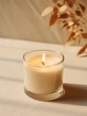 Minimalist burning wax candle in clear glass on natural beige stone background with copy space, styled commercial